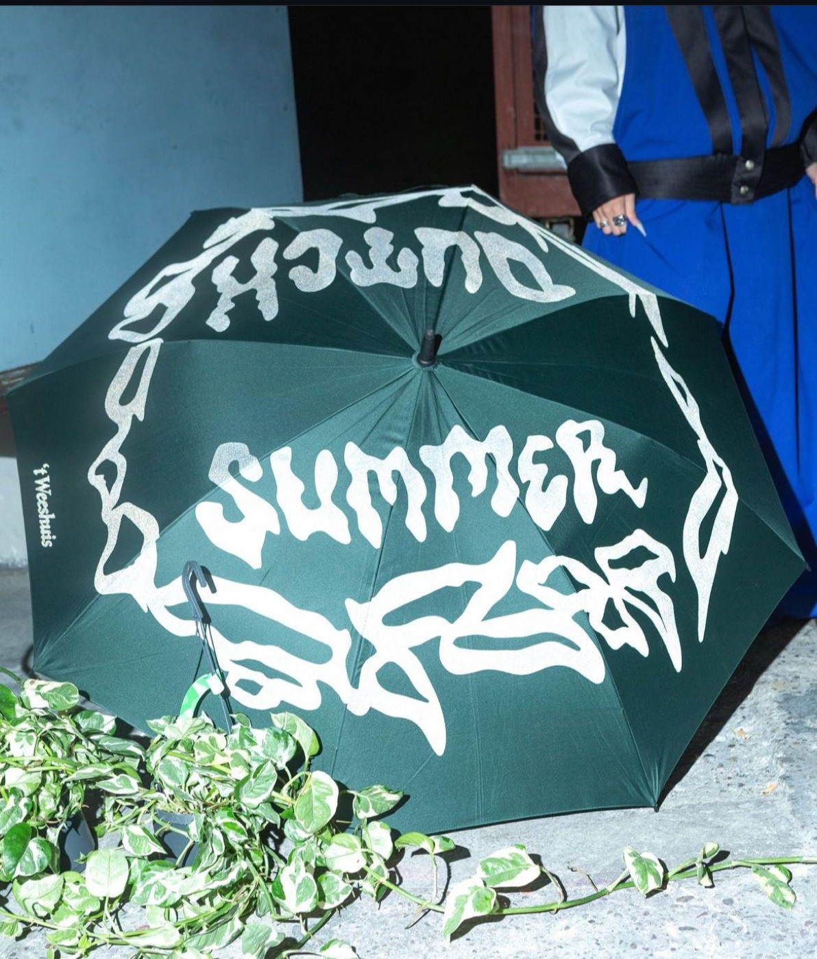 the dutch summer mark printed in white on a dark green umbrella, held open over foliage