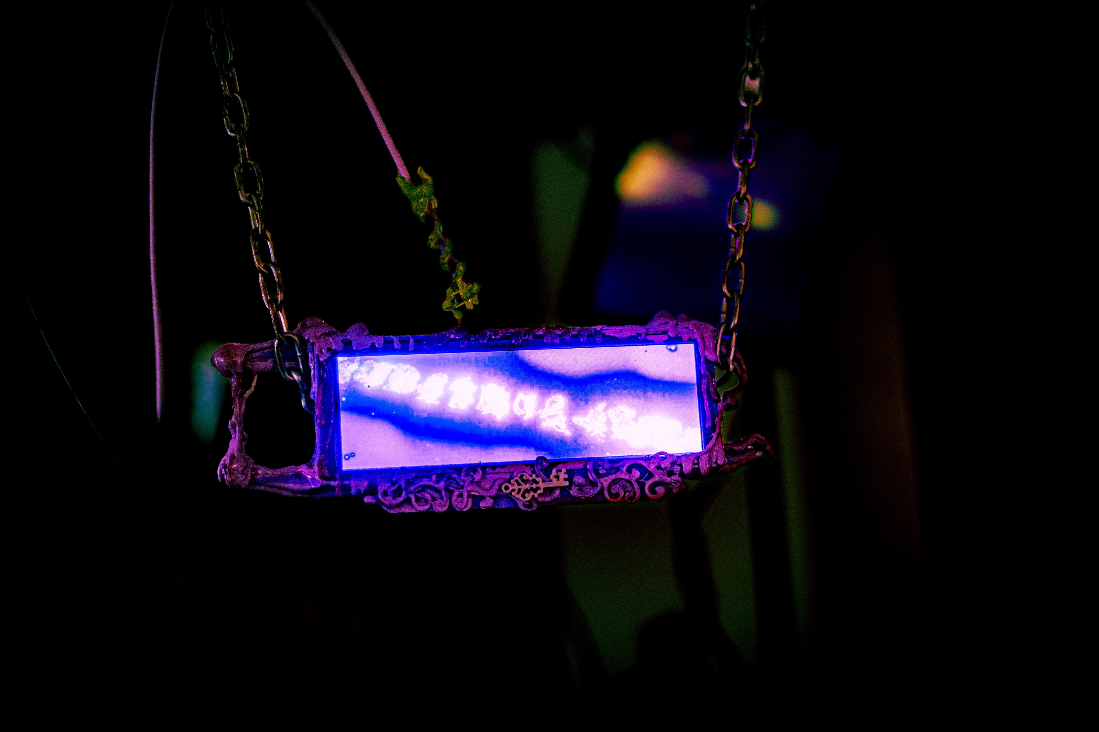 a long letterbox screen in an ornate cast frame dripping with lilac slime, hung on chain, the screen showing a white marbled vein of light running diagonally across a violet field like ink dropped in water
