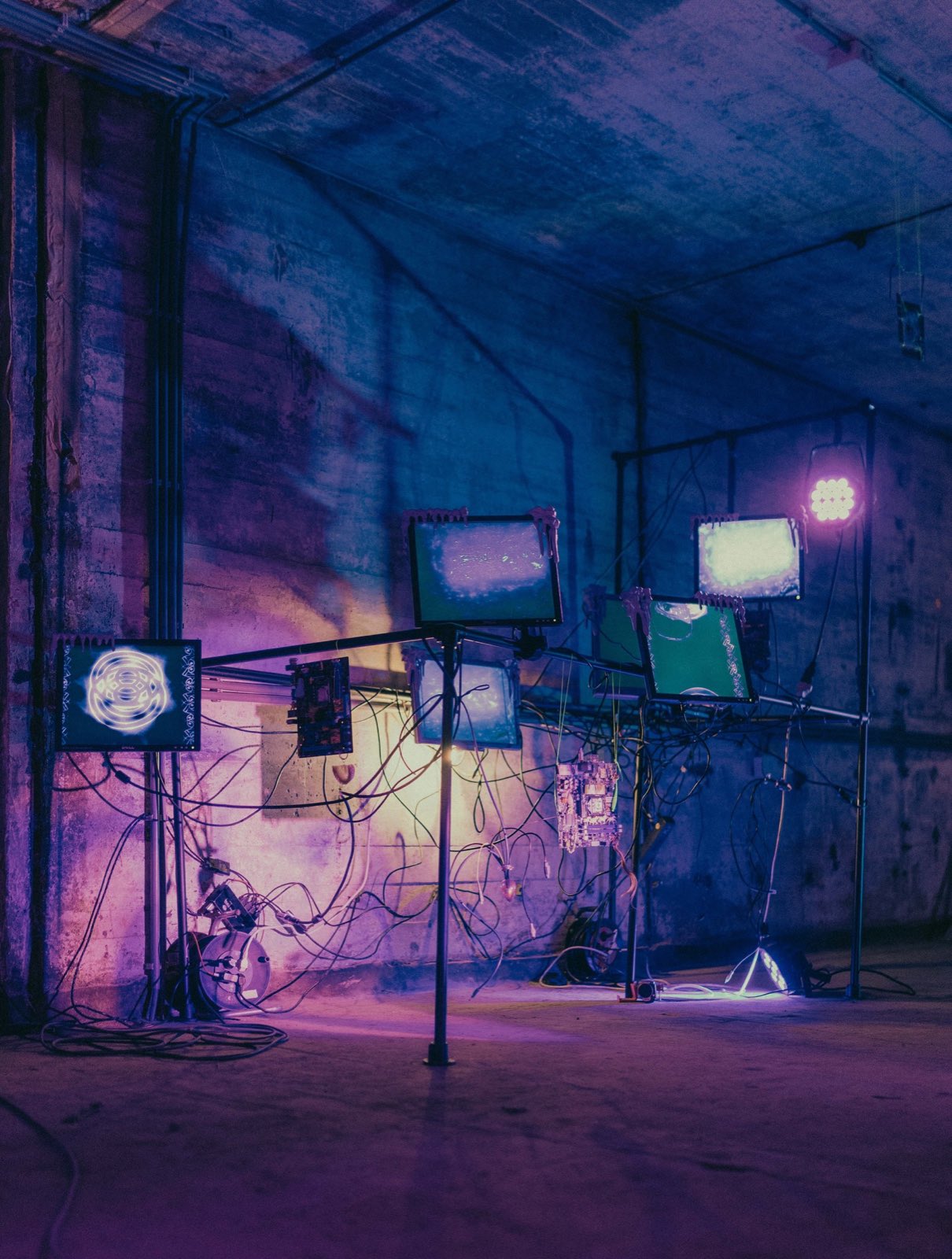 dreaming in the ruins of big tech, salvaged monitors on a scaffold rig in a concrete hall
