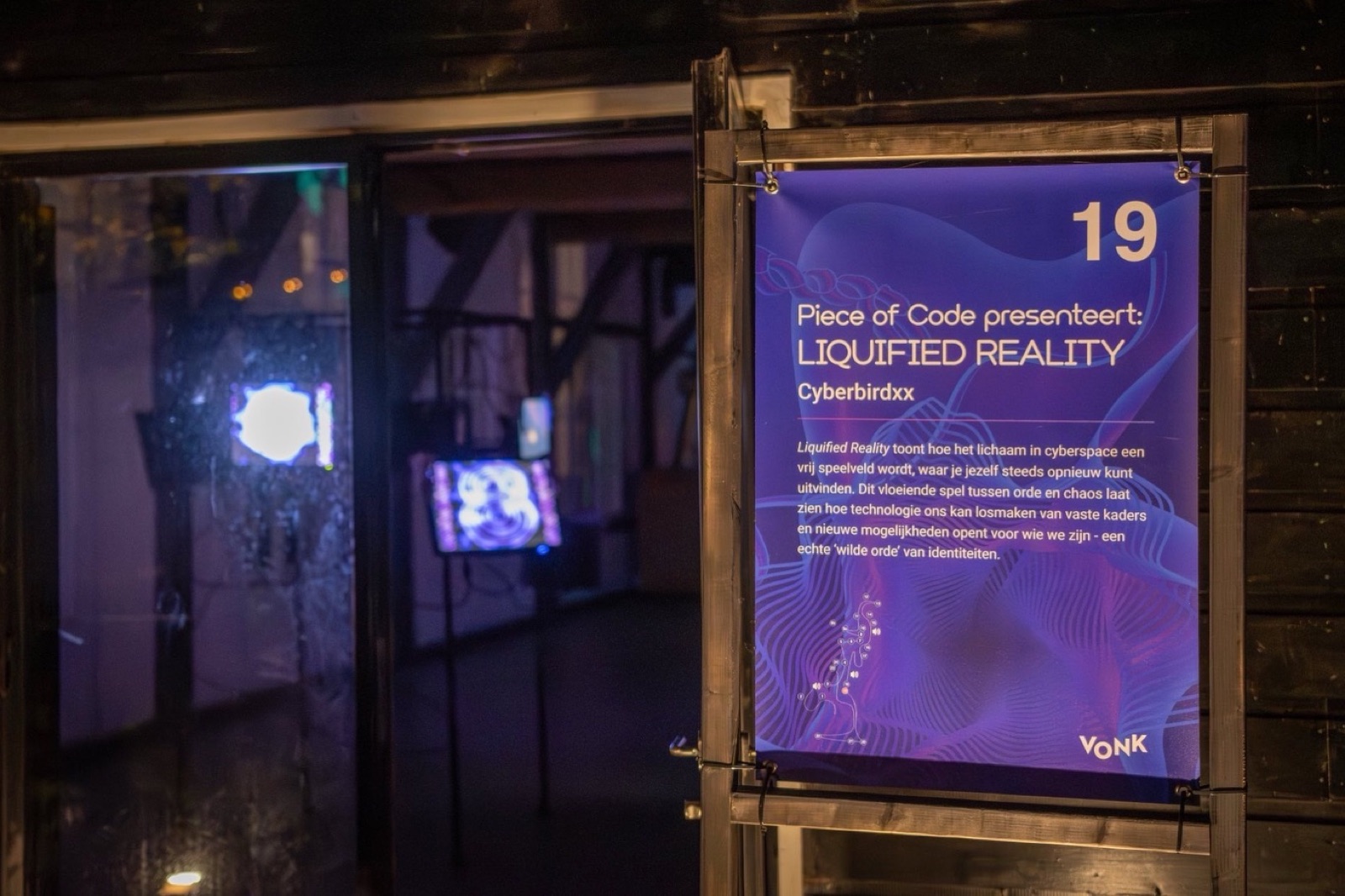 an exhibition wall label beside a doorway into a dark room with two lit screens, printed with the piece's title and cyberbirdxx's name.